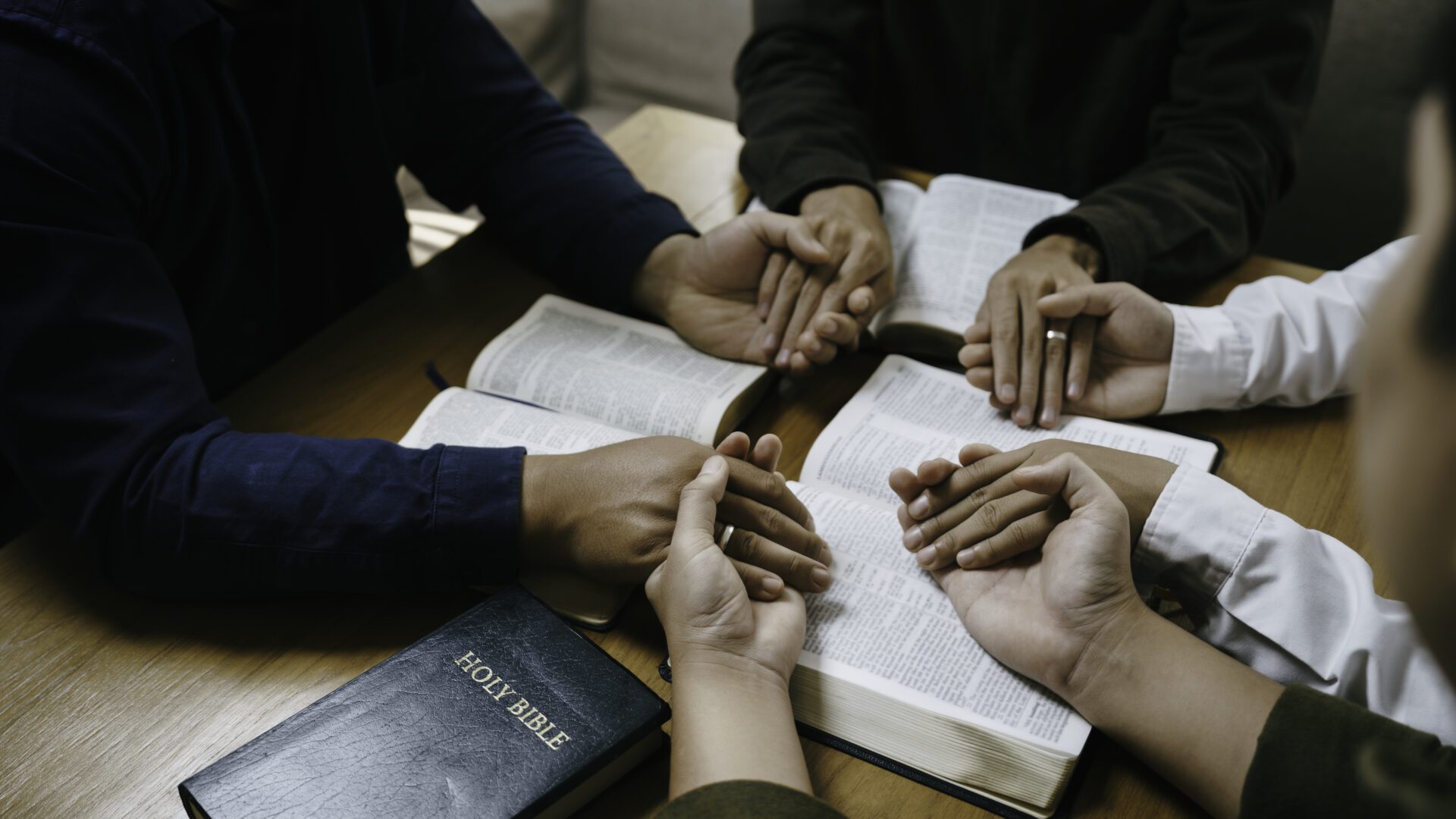 People holding hands, praying with open Bible.